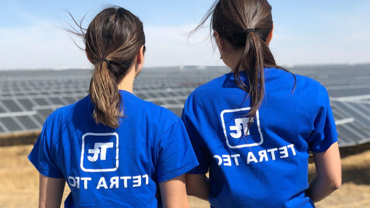 Two women with their backs to the camera wearing blue Tetra Tech shirts look out over a solar farm in Kazakhstan